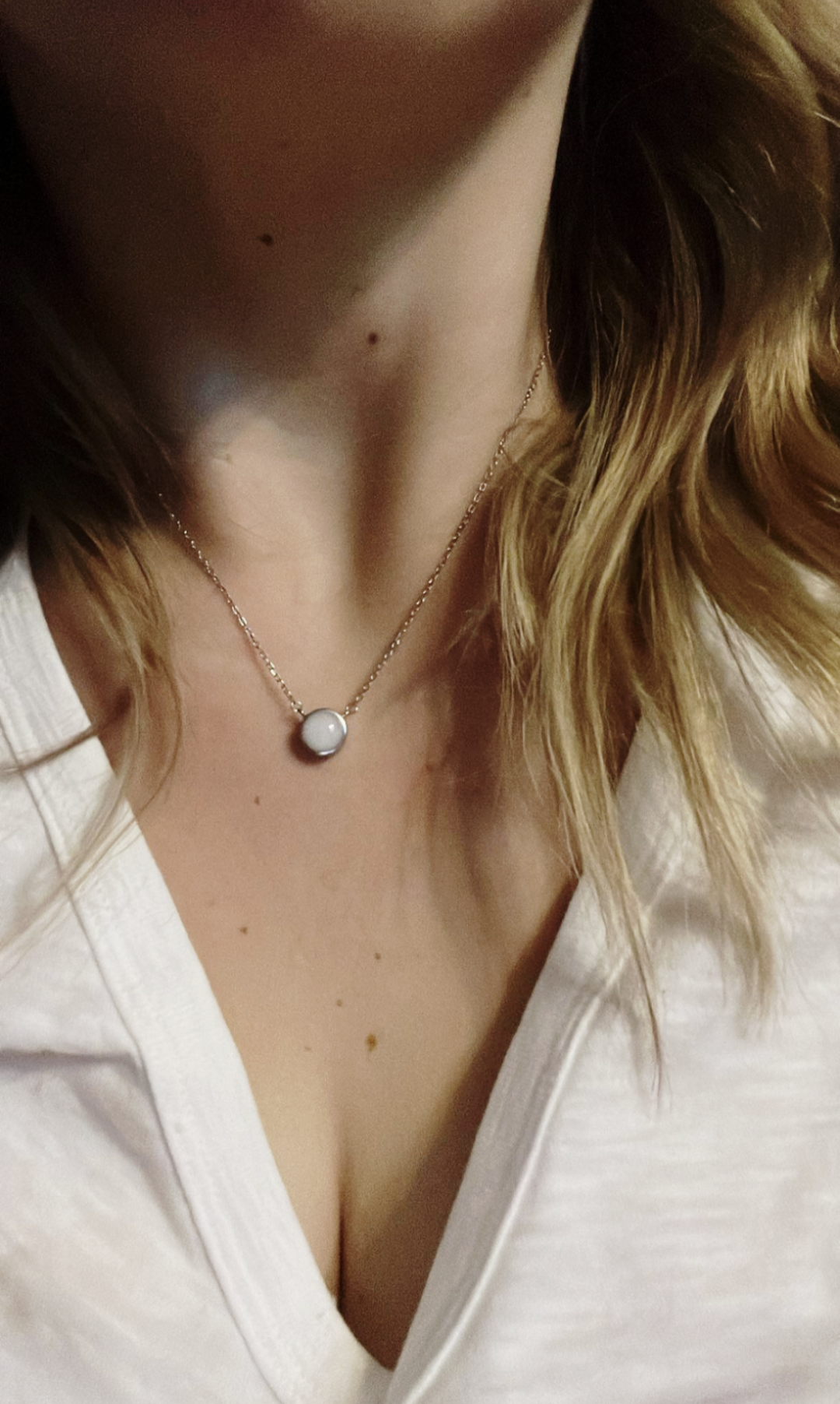 Blond woman wearing a small round breastmilk necklace.