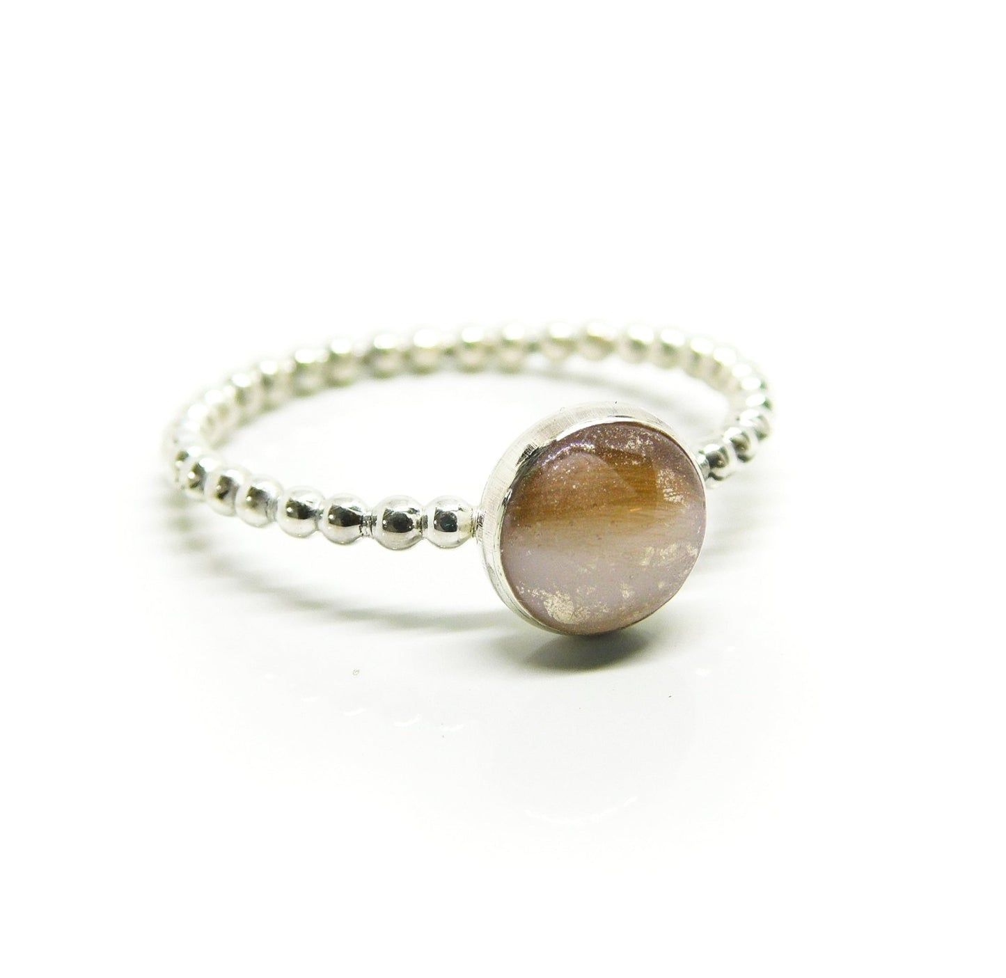 This image shows a delicate sterling silver beaded ring featuring a round, breastmilk stone with a milky white base and brownish inclusions. This could be a breast milk ring, a unique keepsake jewelry piece. A simple yet sentimental sterling silver ring.