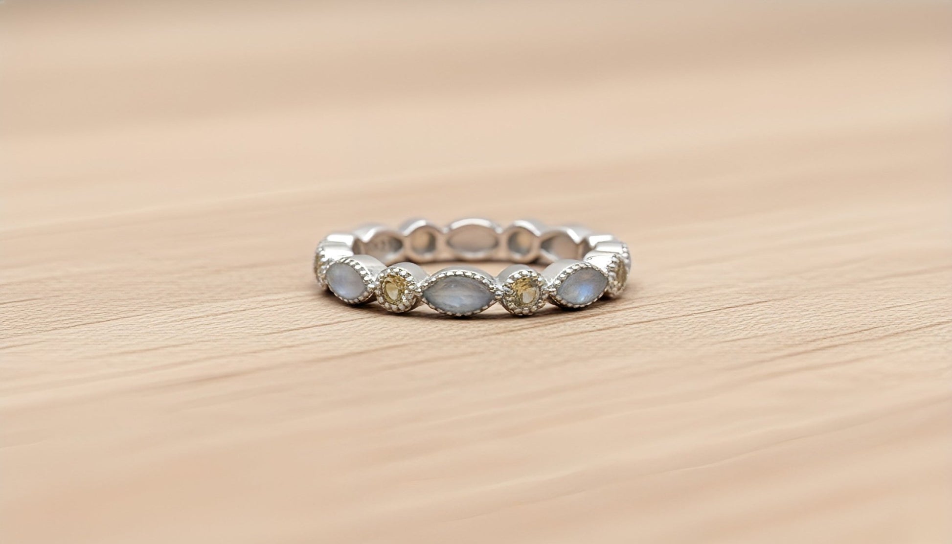 Silver ring with embedded white and yellow stones on a wooden surface