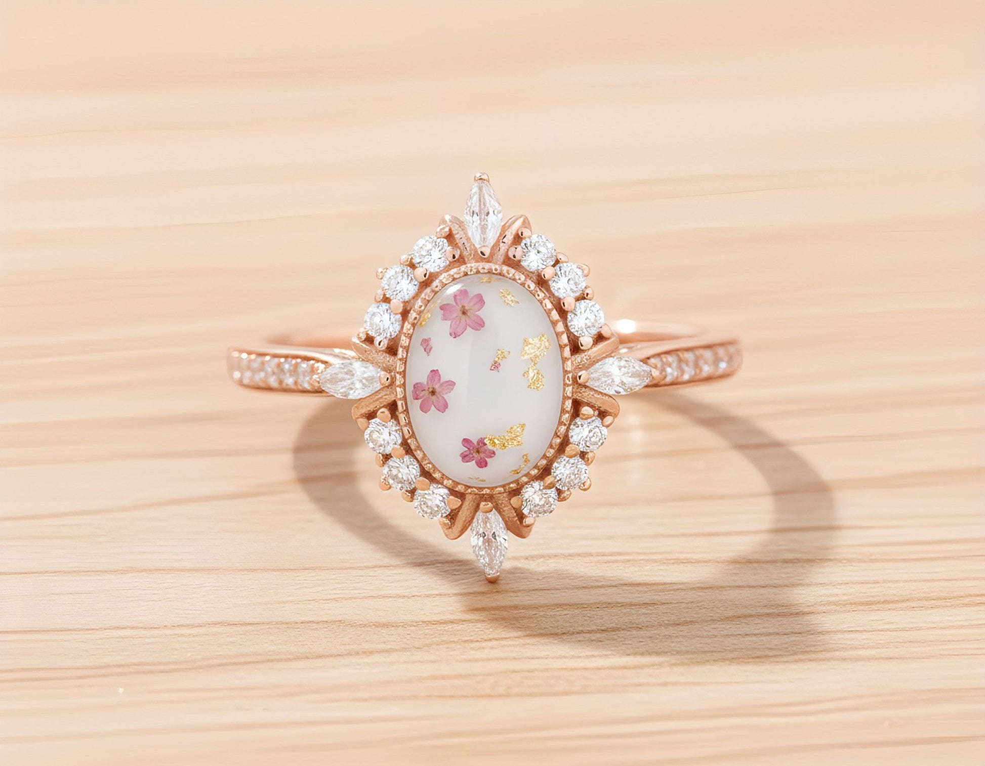 Rose gold ring with a Breastmilk stone with pink flowers and gold flakes on a wooden surface.