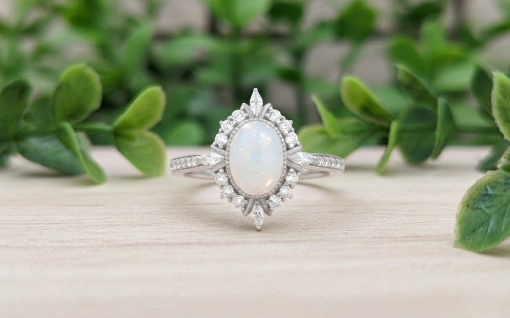 Silver ring with a central breastmilk gemstone on a wooden surface surrounded by green foliage.
Milky Way Spirit & Soul Keepsakes 