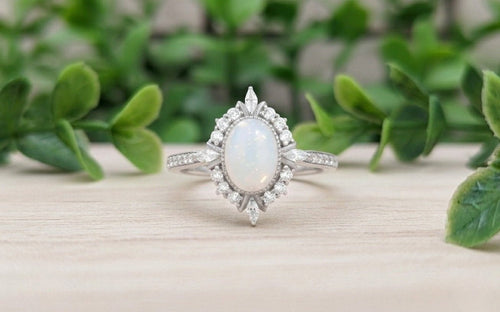 Silver ring with a central breastmilk gemstone on a wooden surface surrounded by green foliage.
Milky Way Spirit & Soul Keepsakes 