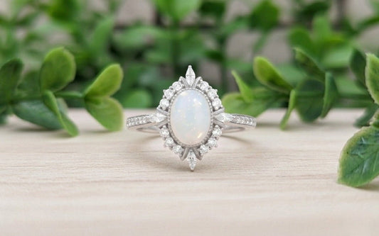 Silver ring with a central breastmilk gemstone on a wooden surface surrounded by green foliage.
Milky Way Spirit & Soul Keepsakes 