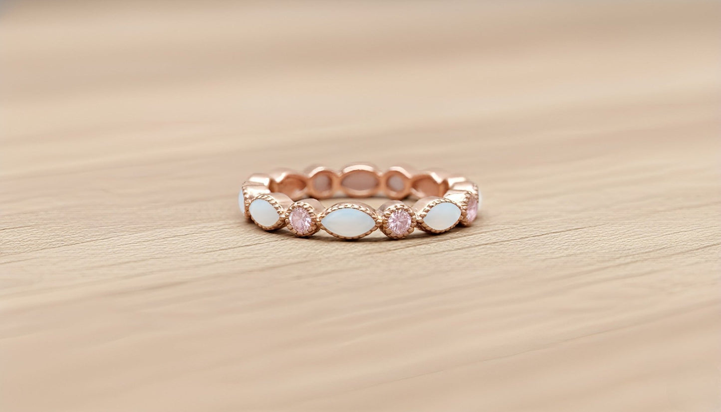 Rose gold ring with pink and white stones on a wooden surface