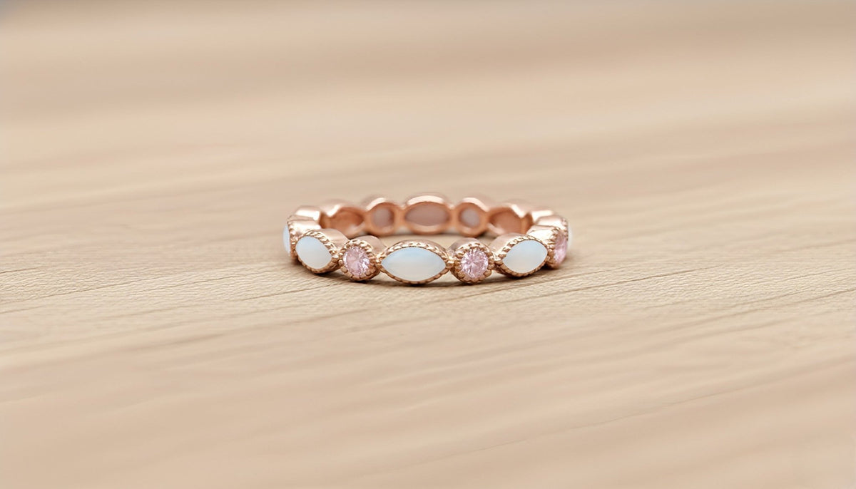Rose gold ring with pink and white stones on a wooden surface