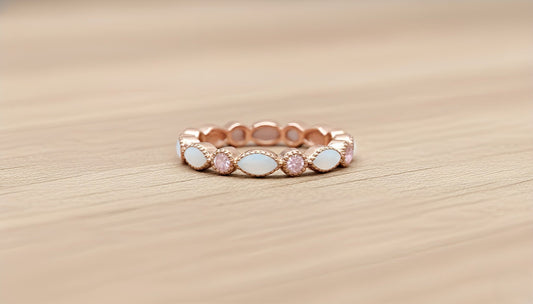 Rose gold ring with pink and white stones on a wooden surface