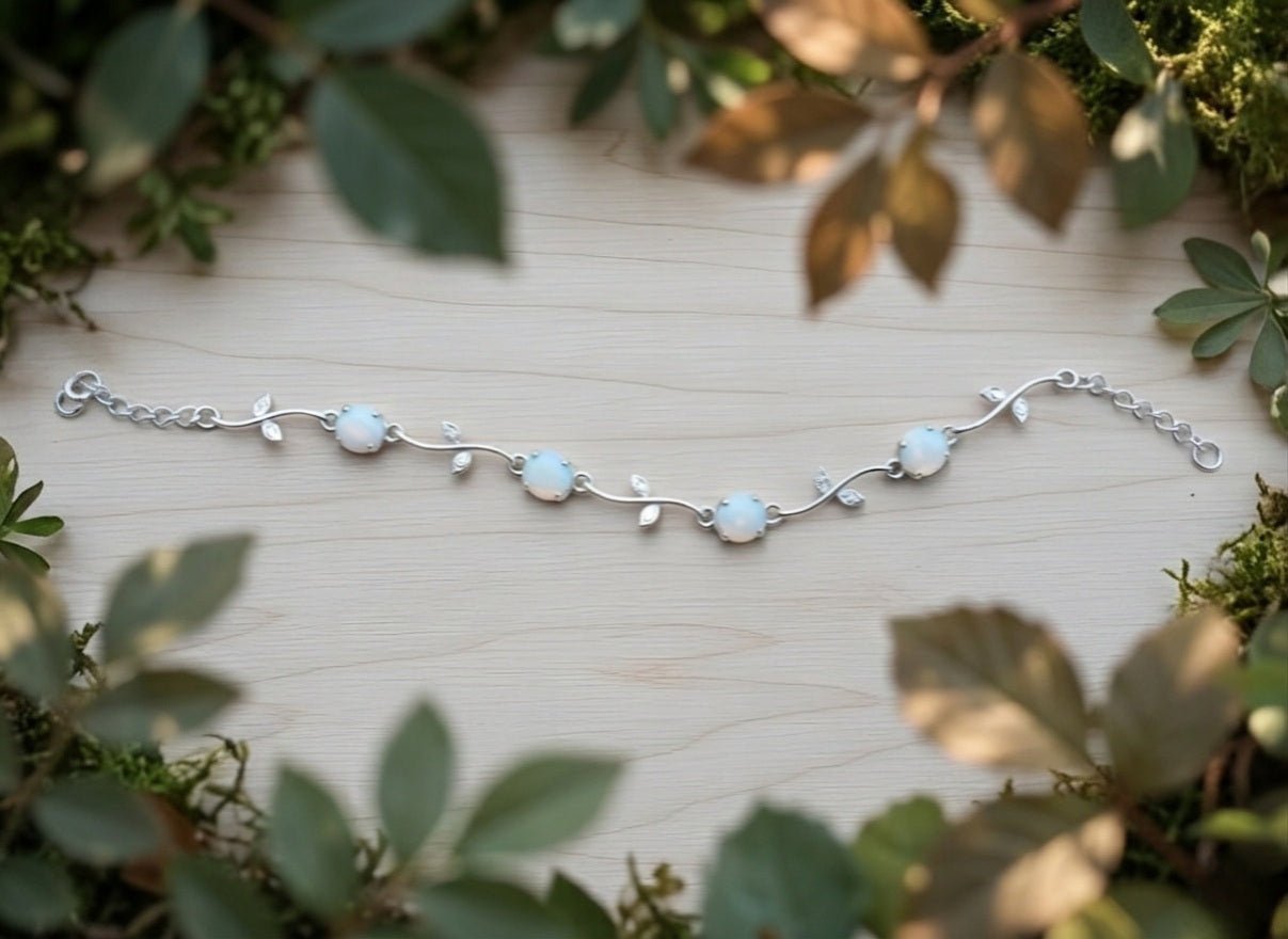 Silver bracelet with opaly milk stones on a wooden surface surrounded by green leaves